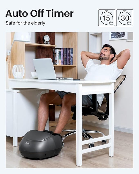 A man sits relaxed in an office chair at a desk with a laptop, leaning back with his hands behind his head. His feet are placed on the Renpho UK Shiatsu Foot Massager Pro + (2nd Generation) that improves circulation with heat. The image includes a text overlay: "Auto Off Timer," "Safe for the elderly," and icons showing 15-minute and 30-minute adjustable functions.